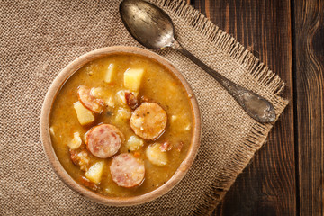 Wooden bowl of split pea soup with sausage and potatoes