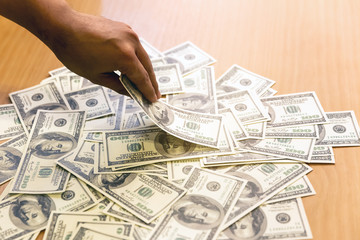 View of money american hundred dollar bill spread on wooden table, someone hand hold money to pay buy something or pay for corruption.
