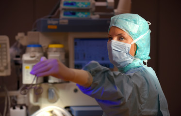 Fototapeta na wymiar A young woman poses in an operation theater fully dressed as a medical theater nurse with a face mask and green sterile medical work clothing.