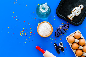 Cooking halloween gingerbread cookies concept. Glazed cookies, ingredients, crockery on blue background top view copy space