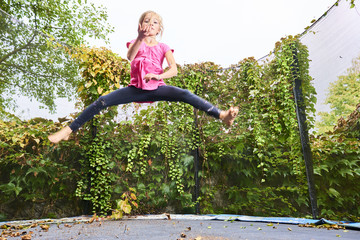 Child girl jumping on trampoline with greenery background