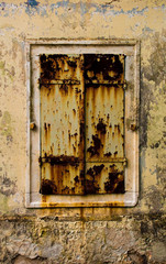 A window covered with rusty shutters in a derelict building in the Croatian hill village of Bale, also called Valle.
