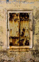A window covered with rusty shutters in a derelict building in the Croatian hill village of Bale, also called Valle.
