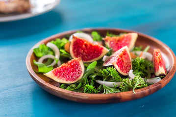 Autumn salad of arugula, figs in a brown earthenware plate on a blue background. top view