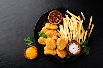 Chicken nuggets and french fries with various sauces on a black background. Top view