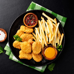 Chicken nuggets and french fries with various sauces on a black background. Top view
