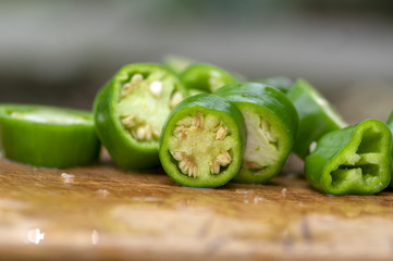 Capsicum annuum Jalapeno chilli hot peppers, group of green sliced fruits on wooden cutting board with seeds