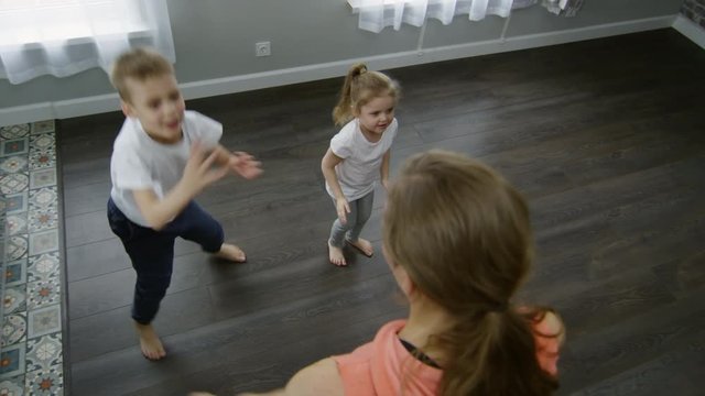High angle shot of mother and little children doing jumping jacks in morning while exercising at home