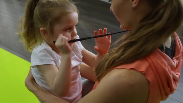 High angle shot of cute preschool-age girl sitting on laps of young mother doing yoga and playing with strings of her sports hoodie