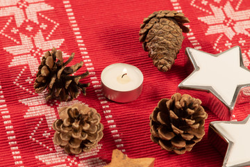 Some pine cones and a burning candle as christmas decoration on red tablecloth