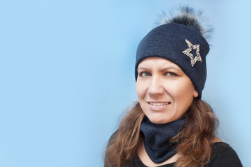 A beautiful woman in a warm winter hat smiles on a blue background