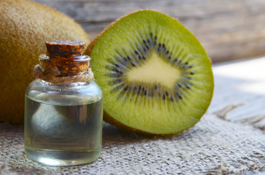 Essential kiwi seed oil in a glass jar with fresh kiwifruit whole and half on old wooden background.Aromatherapy,spa,beauty treatment and bodycare concept.Selective focus.