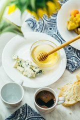  couple of cups with coffee, cheese, honey, baguette and fruit on a light marble table