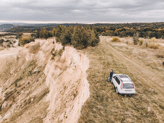 Obraz premium white suv at the top of the hill in autumn overcast weather. man standing near car around wild nature