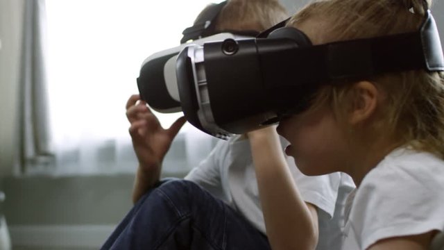 Tilt up shot of cute little boy and girl sitting in VR goggles, then taking them off