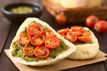 Olive bread roll halves spread with basil pesto and topped with roasted cherry tomato halves, photographed with natural light (Selective Focus on the middle of the first bread roll half)