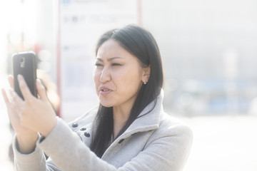 Junge Frau Asiatin kauft Ticket mit Smartphone an einer Haltestelle