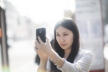 Fototapeta premium Junge Frau Asiatin kauft Ticket mit Smartphone an einer Haltestelle