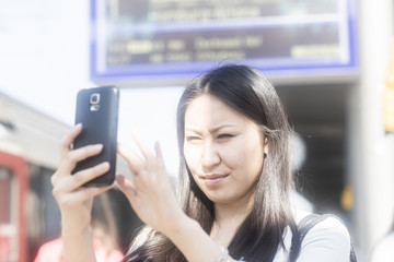 Fototapeta premium Schicke junge Frau Asiatin kauft Ticket mit Smart phone am Bahnhof