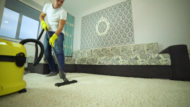 Vacuum cleaner cleans the carpet. A man from a cleaning company works, vacuuming the carpet