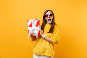 Surprised woman in red eyeglasses holding red box with gift present celebrating, enjoying holiday...