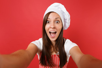 Housewife female chef cook or baker in striped apron, white t-shirt, toque chefs hat isolated on red wall background. Close up housekeeper woman doing taking selfie shot. Mock up copy space concept.