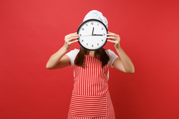 Housewife female chef cook or baker in striped apron white t-shirt toque chefs hat isolated on red wall background. Woman holding in hand in front face round clock hurry up. Mock up copy space concept
