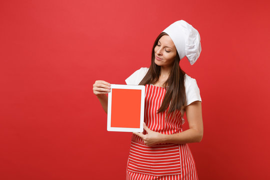 Housewife female chef cook or baker in striped apron white t-shirt toque chefs hat isolated on red wall background. Woman hold tablet pc blank screen for promotional content Mock up copy space concept