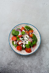 Tomatoes, spinach leaves, red onions and feta cheese salad on light ceramic plate on gray backround. Selective focus. Top view.