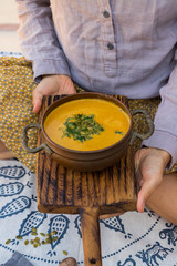 Woman hands holds pumpkin curry creamy soup with coconut milk, parsley. Sweet orange hot pumpkin soup in vintage pot or bowl.