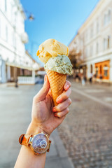 Woman Holding Green Pistachio And Yellow Melon Ice Cream Cone In Hand