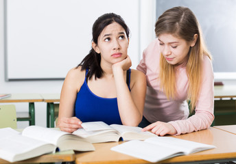 Young girl is helping her girlfriend with writing text in the classroom