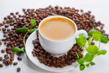 white cup of coffee on a background of scattered coffee beans on a white background