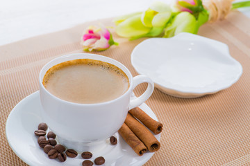 white cup of coffee on a background of scattered flower buds on a white background
