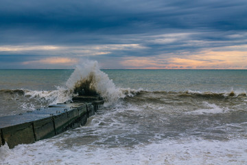 Waves hit the stone sea pier. Splashes scatter in all directions