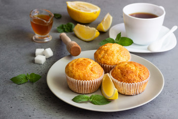 Homemade lemon muffins with honey, mint and cup of tea for breakfast on a concrete background