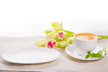 white cup of coffee on a background of scattered flower buds on a white background