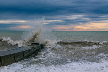 Waves hit the stone sea pier. Splashes scatter in all directions