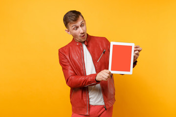 Portrait vogue fun young man in red leather jacket, t-shirt hold tablet pc pad with blank empty screen isolated on bright yellow background. People sincere emotions lifestyle concept. Advertising area