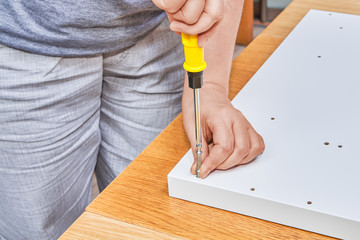 Installer screws fastening furniture screw into white chipboard.