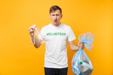 Man in t-shirt volunteer, trash bag isolated on yellow background. Voluntary free assistance help,...