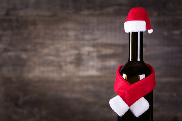 Wine bottle decarated with santa claus hat and scarf on wooden background