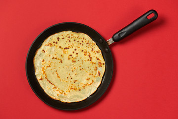 Crepe closeup, thin pancake on a frying pan, red background
