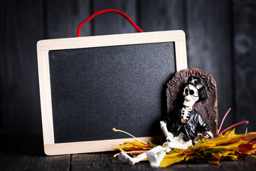 Halloween toy of skeleton with grave and chalkboard on wooden background