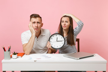 Two young fun shocked business woman man colleagues sit work at white desk with clock, laptop...