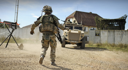 Army soldier directs armoured personnel vehicles in a desert type environment