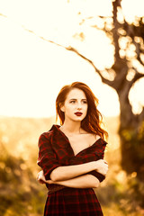 Beautiful girl in plaid dress on sunset at countryside