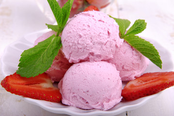 Strawberry ice cream garnished with mint and berries on a white plate on a wooden background.