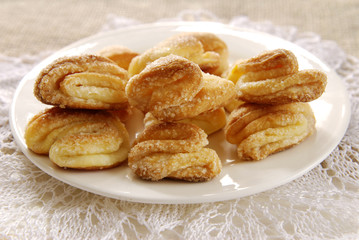 Homemade cookies with cream cheese on a white plate on a lacy napkin on a light wooden background.