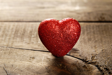 Red heart dotted with sparkles on a dark wooden background.
